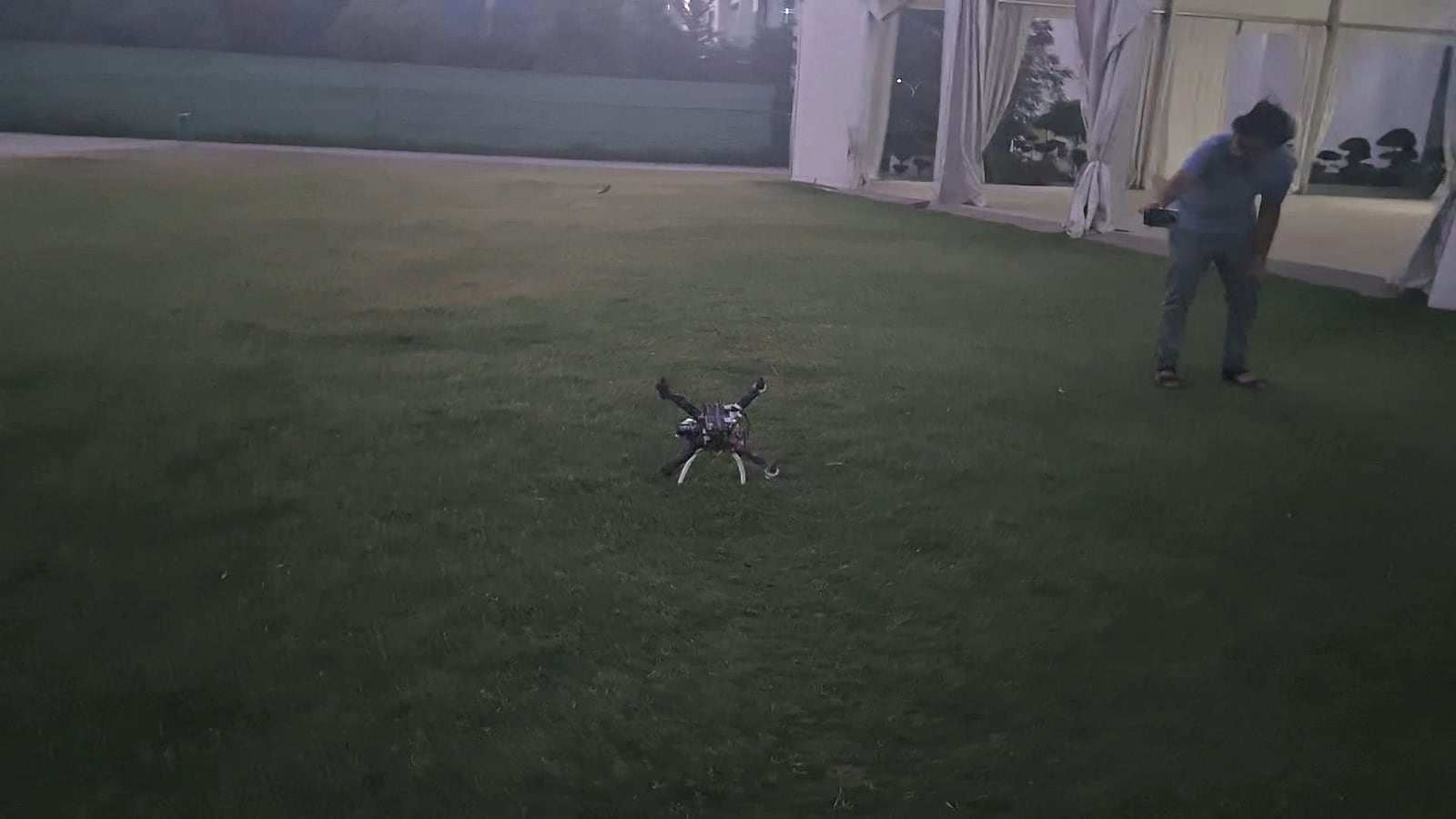 The ANAV quadcopter on a grass field at night, with a pilot holding a transmitter in the background.